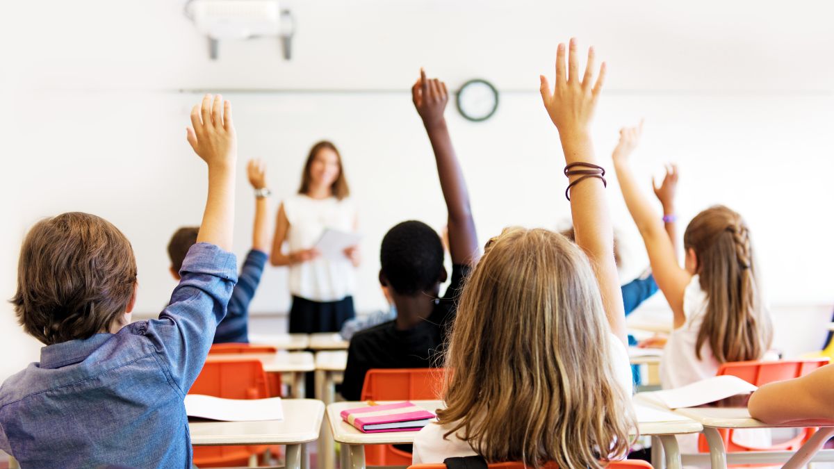 school kids in classroom raising their hands